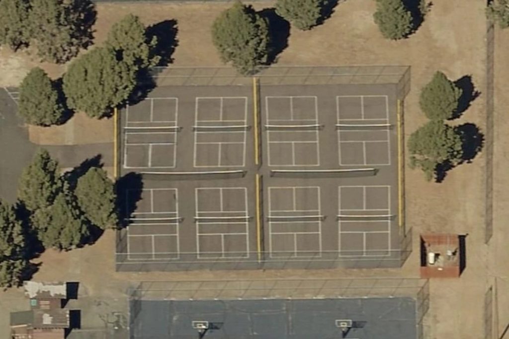 Aerial view of multiple fenced tennis courts in a mountain park setting surrounded by trees and open dry landscape in Big Bear Lake.