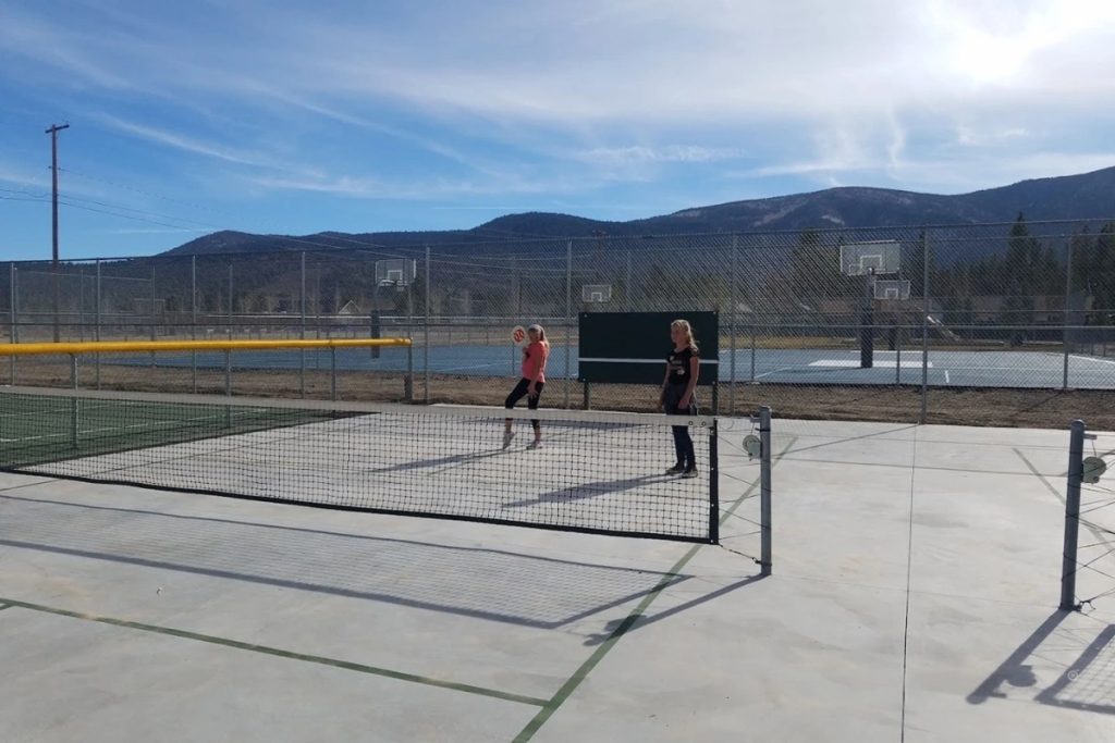 Players playing pickleball on an outdoor court with fencing, mountain scenery, and clear skies at Erwin Lake Tennis Ranch.