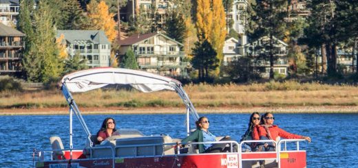 Red and white pontoon boat with people enjoying a relaxing outing at Big Bear Lake, surrounded by scenic forested hills.