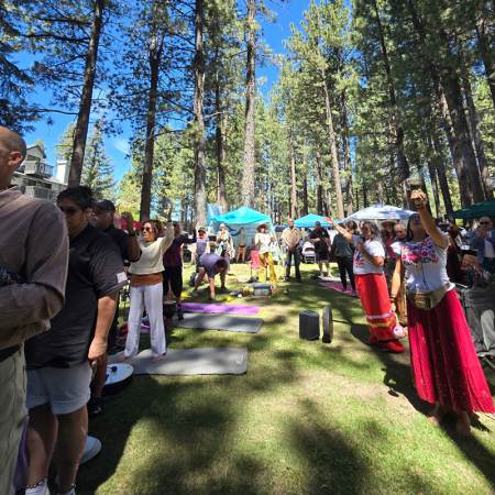 Visitors practicing yoga outdoors during a wellness festival surrounded by trees and nature