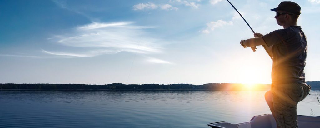 A man fishes from a boat on Big Bear Lake as the sun sets in the background.