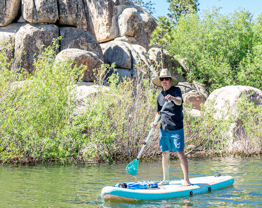 Man stand-up paddleboarding on a lake near rocky shoreline with scenic outdoor adventure and clear water views