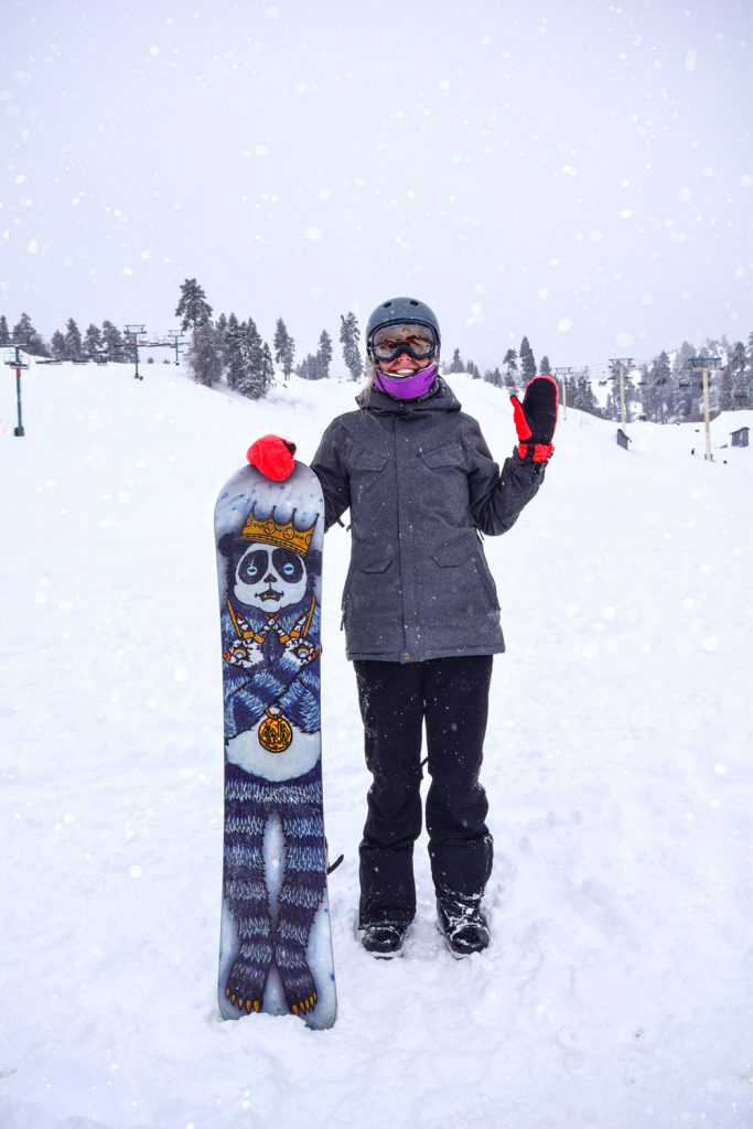 Snowboarder posing with a decorated snowboard in snowfall at Big Bear.