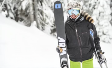 A skier in winter gear holds skis on a snowy slope at Big Bear.