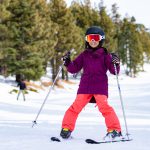 A child in a purple jacket and orange pants skis on a snowy slope at Big Bear.