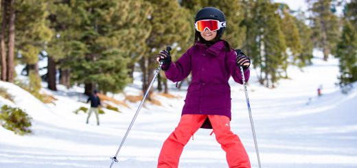 A child in a purple jacket and orange pants skis on a snowy slope at Big Bear.