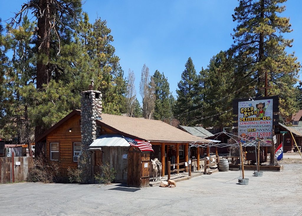 Rustic exterior view of Gold Rush Mining Co with a cabin building, pine trees, and outdoor mining attraction area in Big Bear