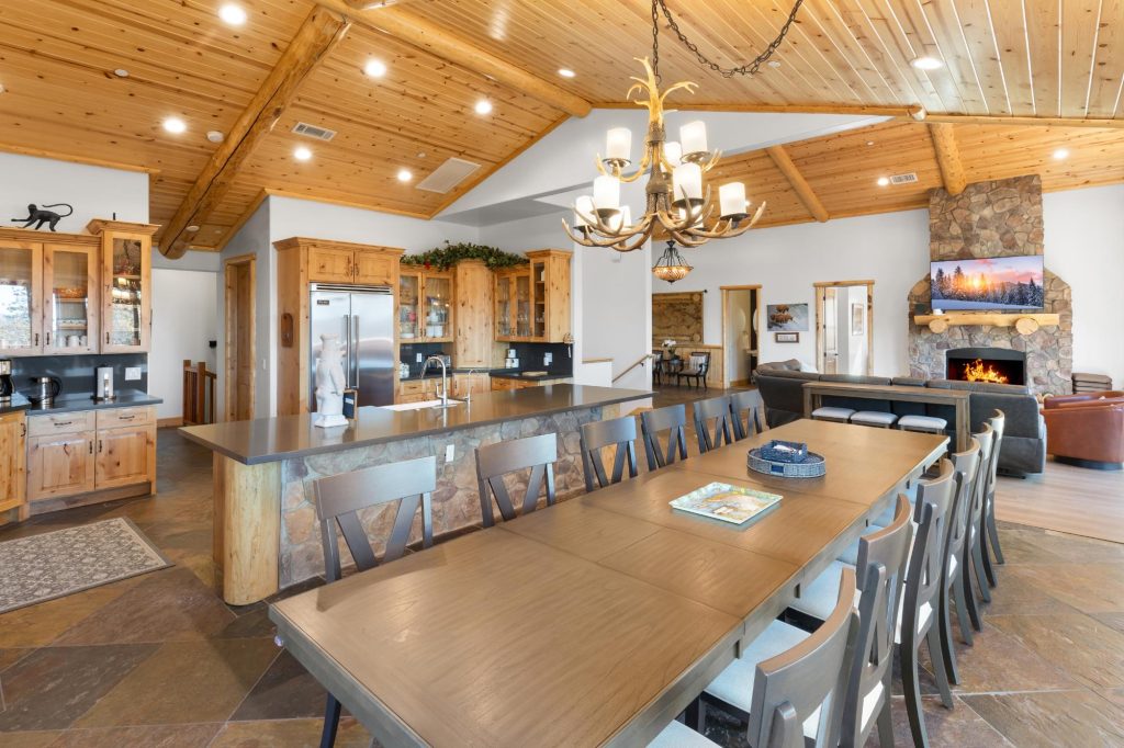Large kitchen and dining area with stone island, wood cabinetry, and fireplace in a mountain lodge