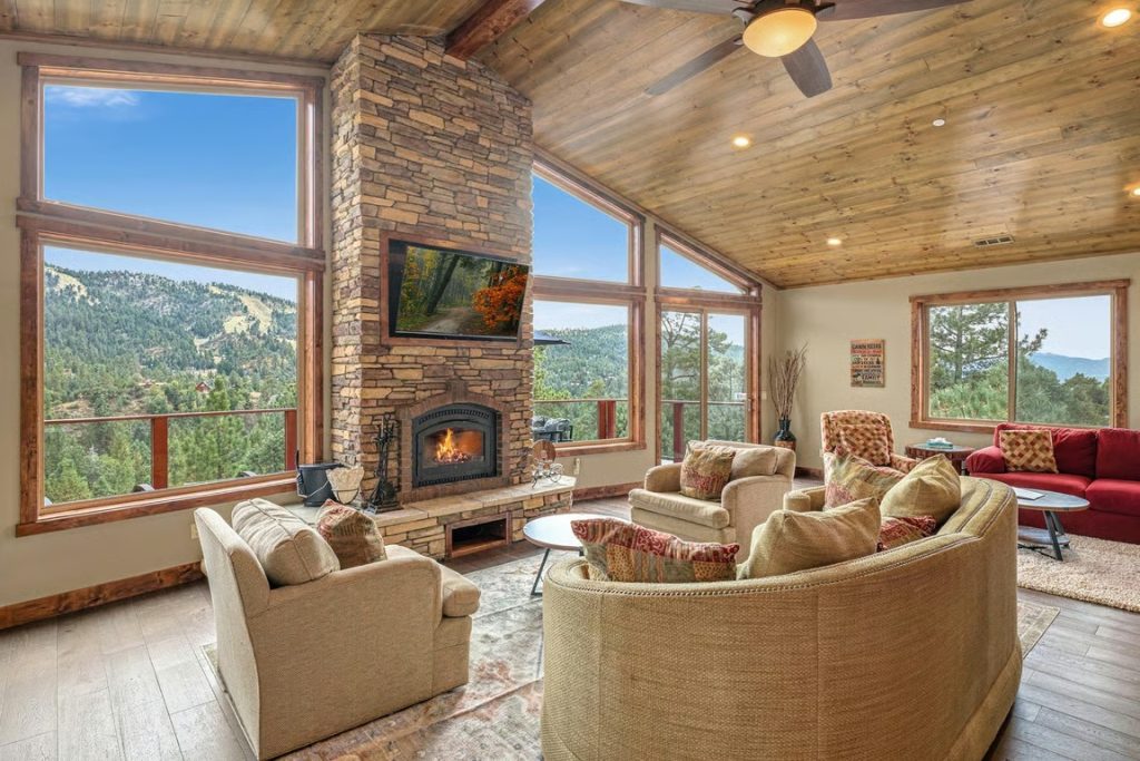 Spacious Gray Wolf Lodge living room with stone fireplace, wood ceilings, large windows, and mountain views