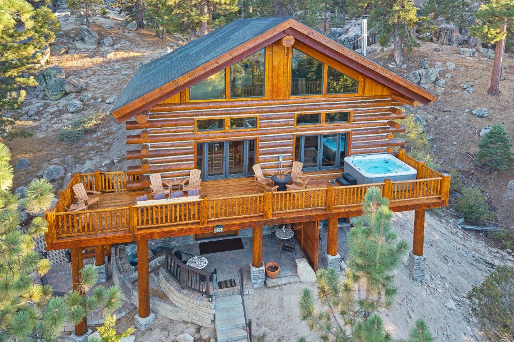 Aerial view of Grinhart Cabin featuring a rustic log exterior, spacious deck, outdoor seating, and mountain forest surroundings