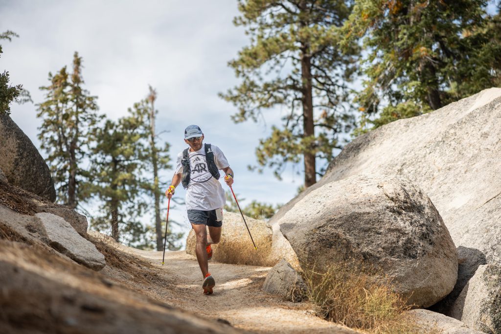 A runner with poles navigates a rocky, tree-lined trail during the Kodiak Ultra Marathons in Big Bear.
