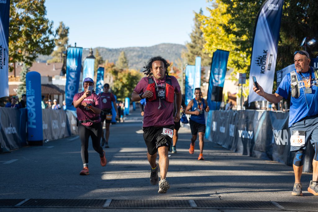 Runners approach the finish line of the Kodiak Ultra Marathons in Big Bear, passing by event banners and spectators.
