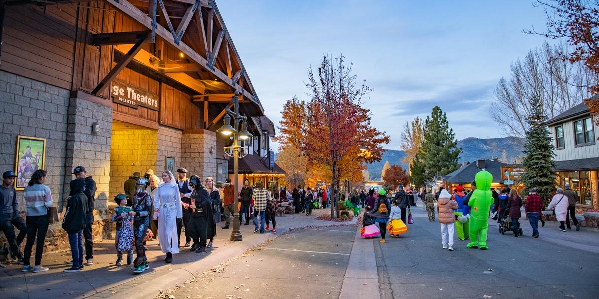 Halloween in the Village in Big Bear with people in costumes walking down the street with fall trees behind
