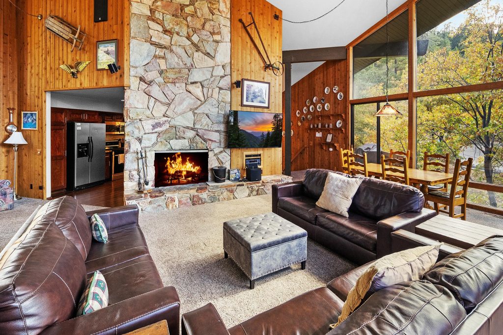 Mountain cabin living room with leather seating, stone fireplace, and large picture windows