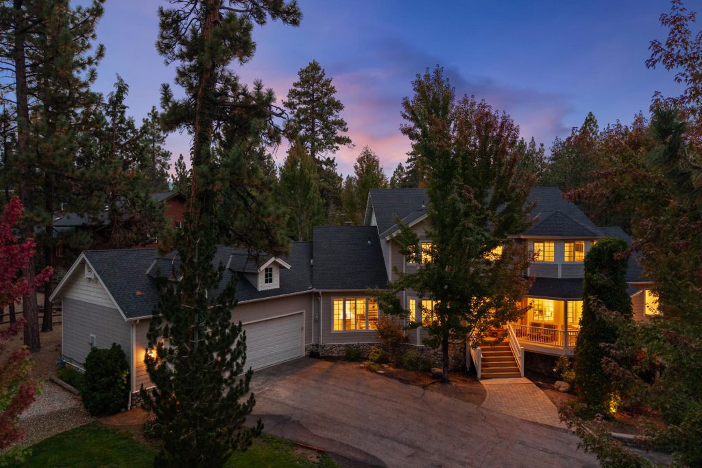The Hidden Estate Big Bear exterior of home hidden in the pine trees 2-story with lights on a dusk