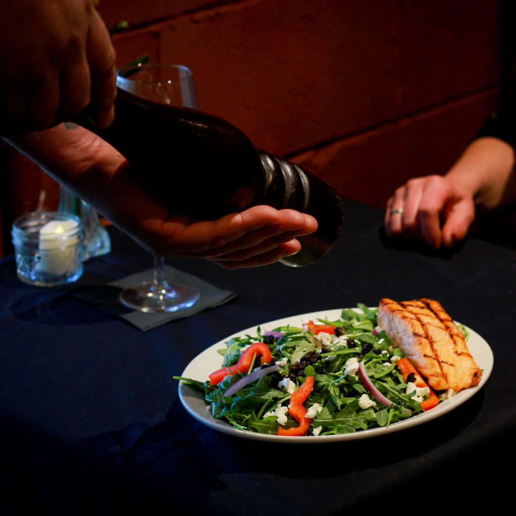A waiter is shown adding pepper to a grilled salmon salad at a restaurant in Big Bear.