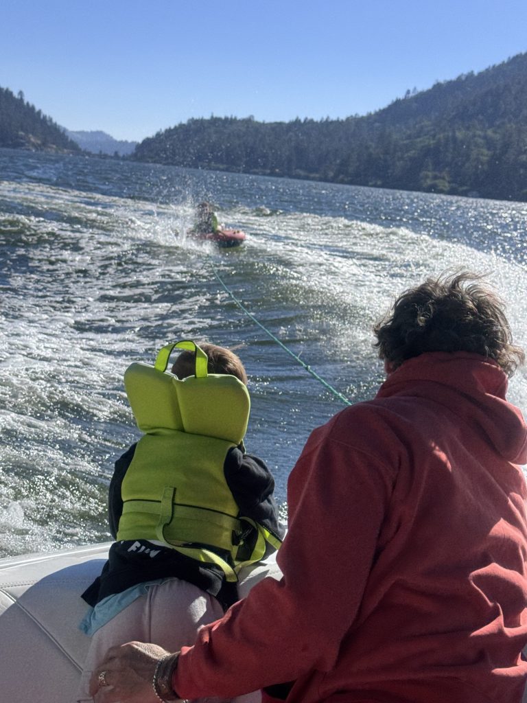 Family enjoying a tubing adventure behind a boat on Big Bear Lake while wearing life jackets.
