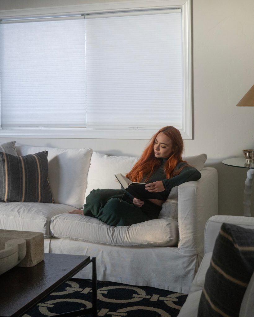 Person relaxing on a comfortable sofa while reading a book in a bright and peaceful cabin living space