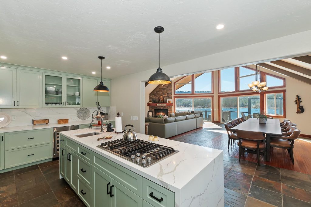 Modern kitchen and great room featuring a large island, dining area, fireplace, and scenic lake views through wide windows