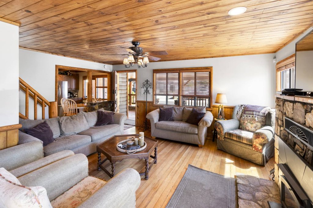 Cozy cabin living room with wood ceiling, stone fireplace, comfortable seating, and rustic mountain home design