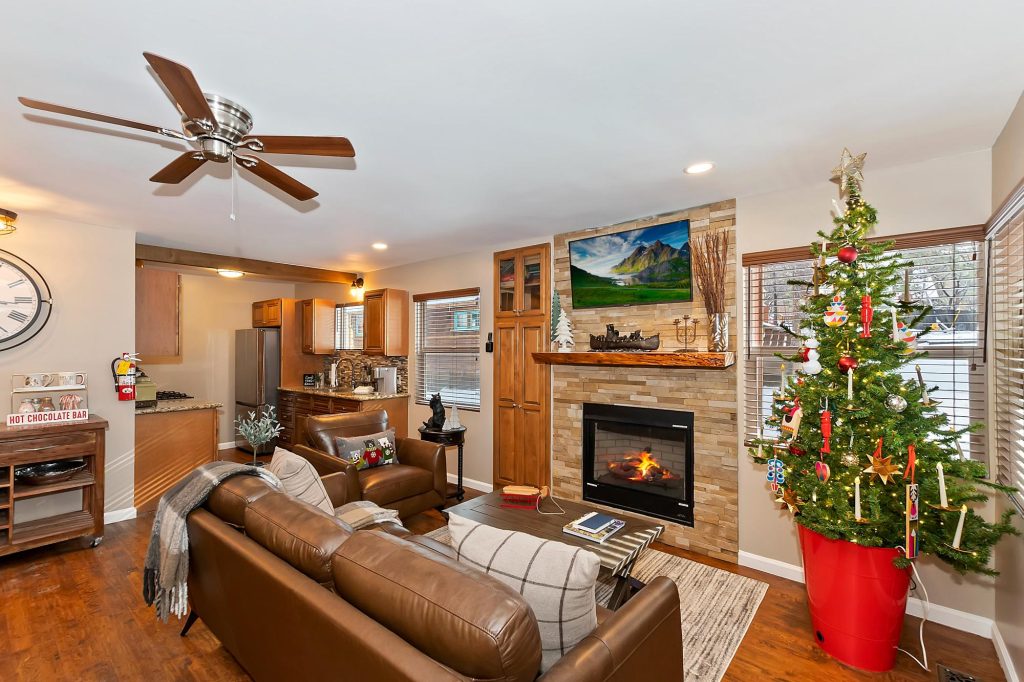Cozy luxury cabin living room with stone fireplace, Christmas tree decoration, leather seating, and warm mountain lodge interior
