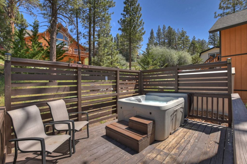 Outdoor jacuzzi deck at Knotty by Nature cabin surrounded by pine trees, comfortable seating, and a peaceful mountain setting