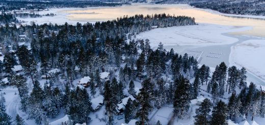 Snow-covered Big Bear Lake and surrounding forest are captured from above, highlighting the tranquil winter scenery.