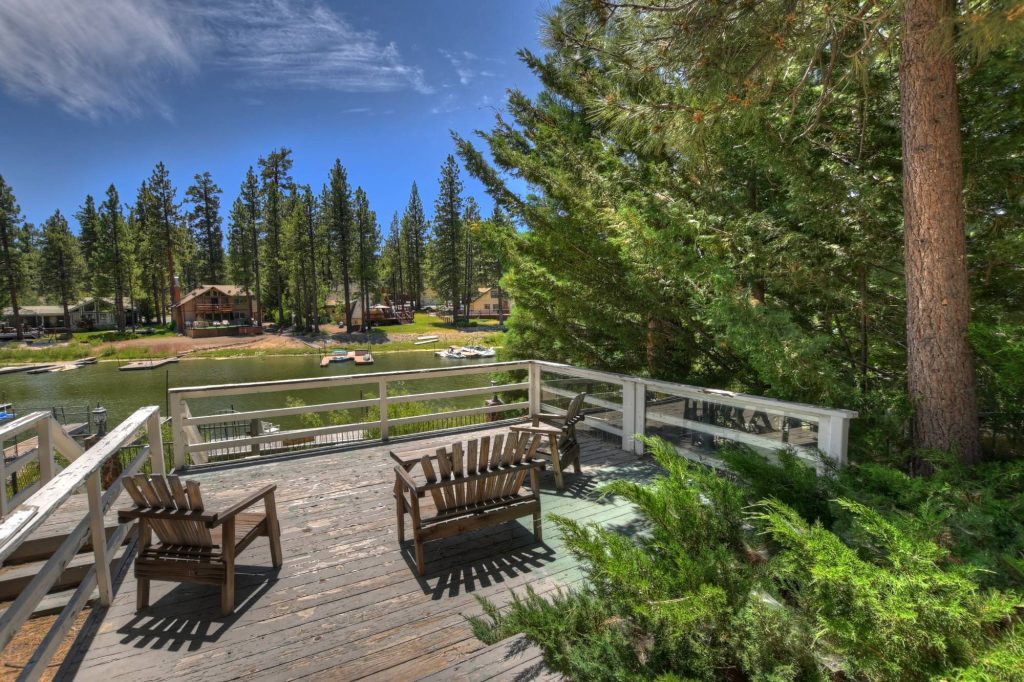 Lakeside backyard deck at Lagunita Shores featuring seating, pine trees, and peaceful waterfront views in Big Bear Lake