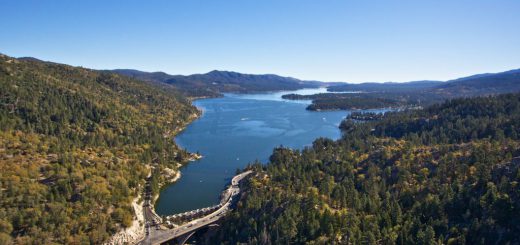 Aerial view of Lake Ariel in Big Bear, surrounded by lush green trees and reflecting the clear blue sky.