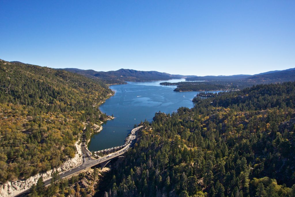 Aerial view of Lake Ariel in Big Bear, surrounded by lush green trees and reflecting the clear blue sky.