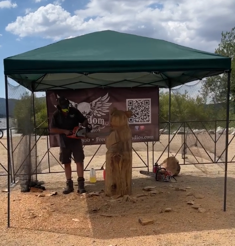 Artist creating a live wood carving sculpture under a canopy at the Lakefest event