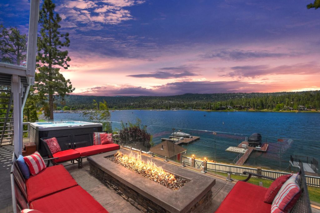 Lakefront backyard with red seating, fire pit, hot tub, and scenic lake view at sunset