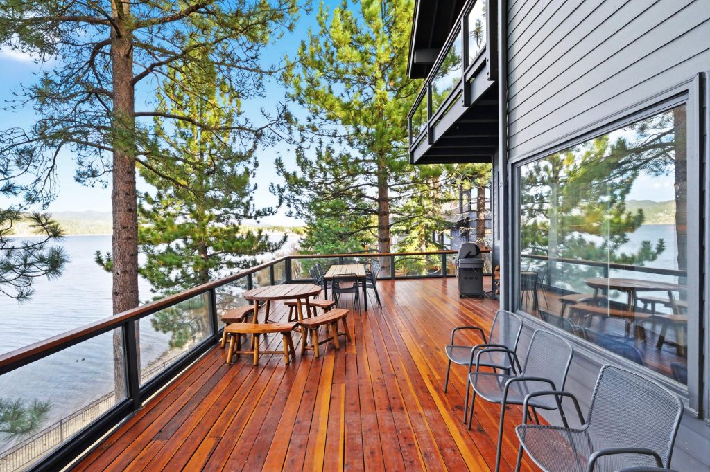 Lakefront backyard view with wooden deck, seating, and scenic lake and tree backdrop