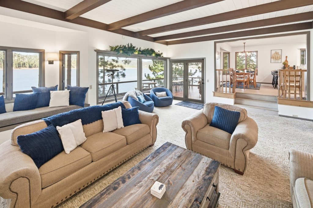 Spacious lakefront living room with large windows, beige couches, blue accents, and scenic lake view