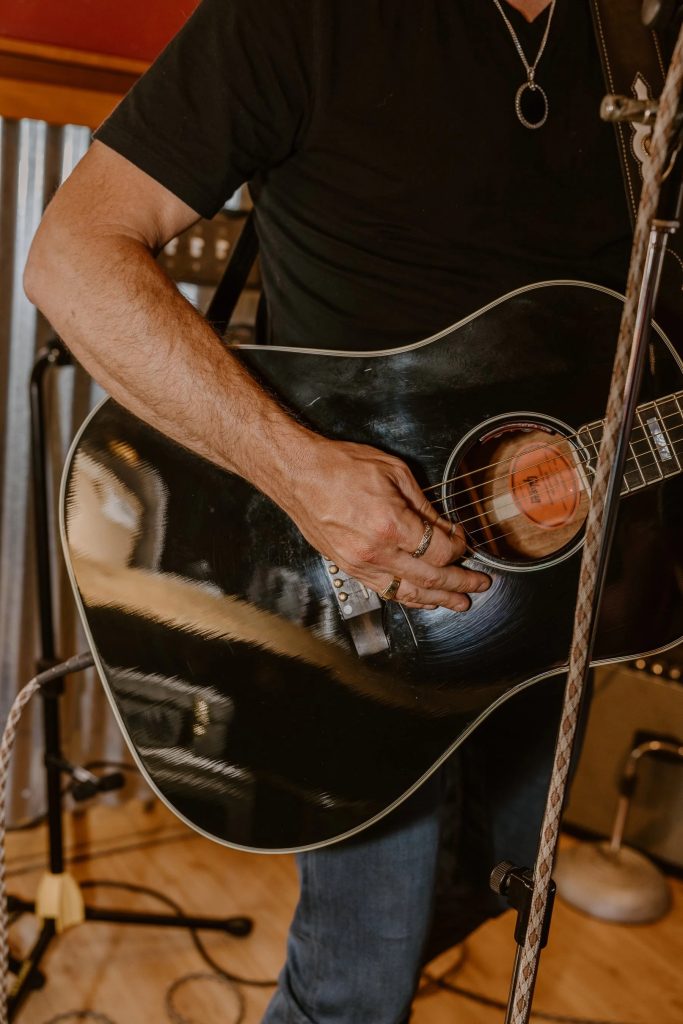 Close-up view of musician playing a black acoustic guitar during a live performance