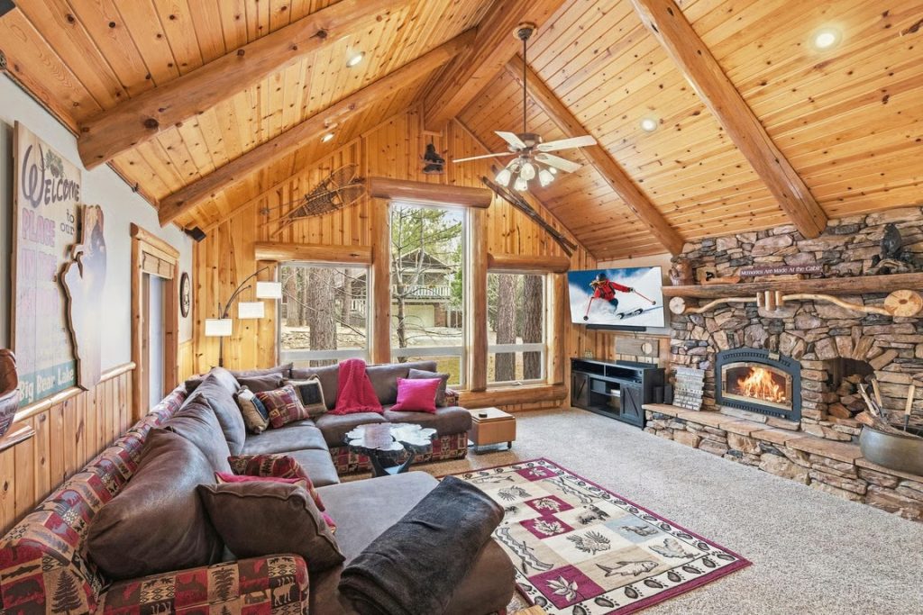 Rustic Big Bear lodge living room with a stone fireplace, wood-paneled walls, cozy sectional seating, and mountain decor