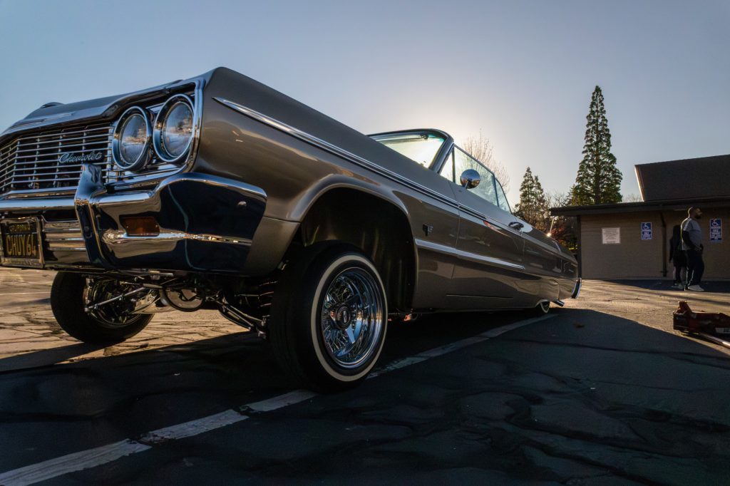 Classic Chevrolet lowrider with raised suspension parked in a parking lot during sunset.