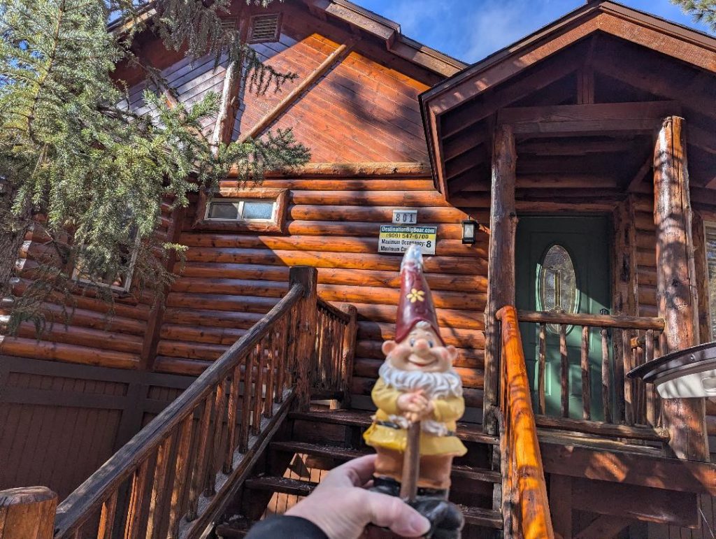 Entrance of Bear Butte Lodge with a cheerful garden gnome and rustic log cabin charm.