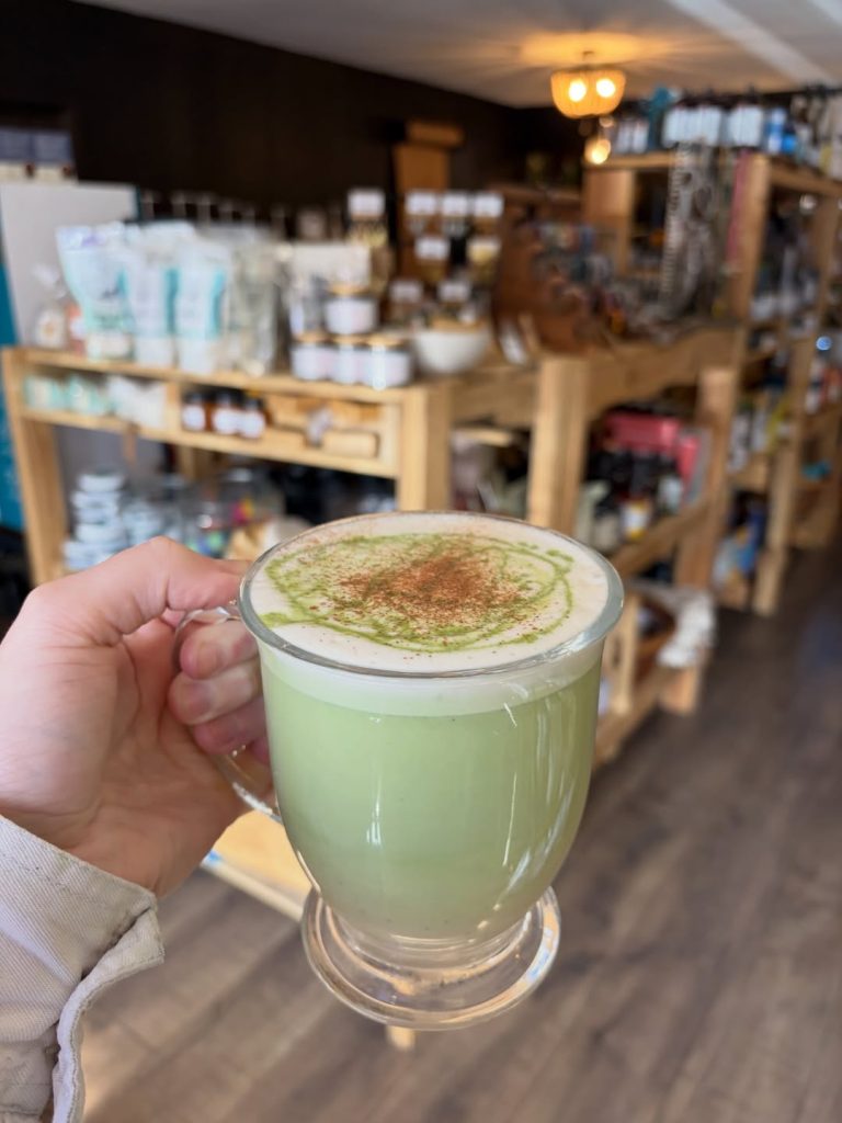 Creamy matcha latte served in a glass mug inside a cozy café with artisan products displayed in the background.
