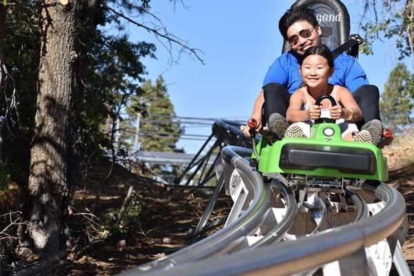 Man and young girl smiling while riding the green Mineshaft Coaster cart through the forest at Big Bear.