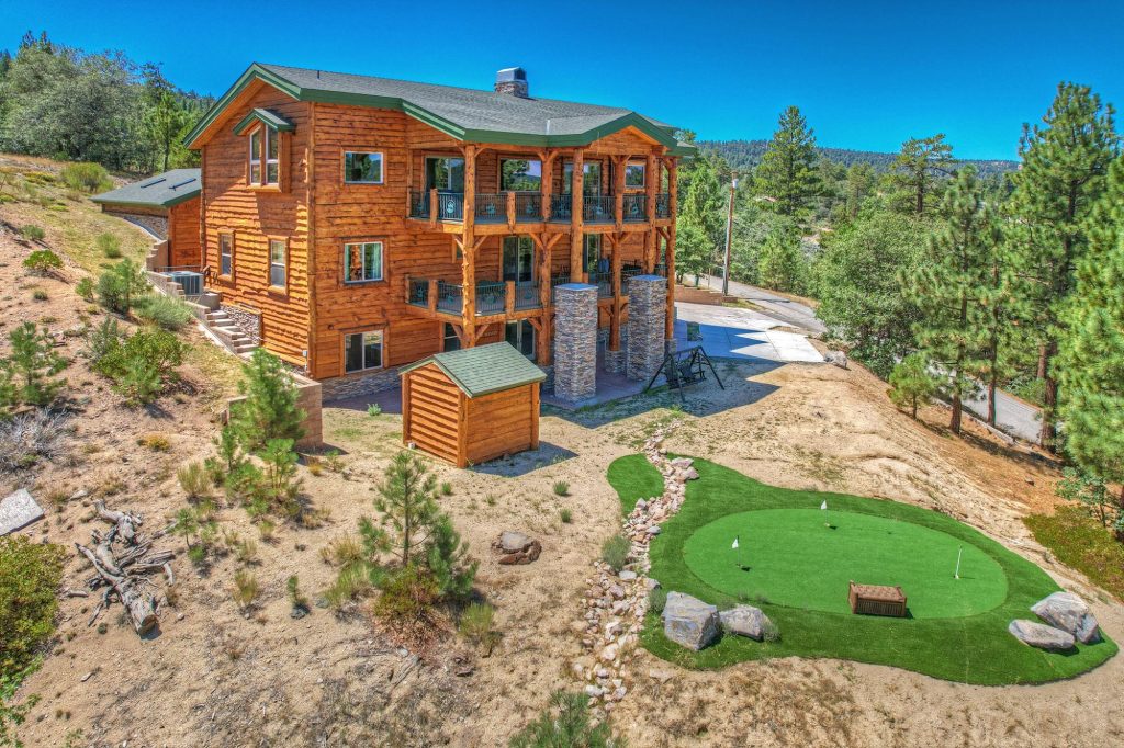 Large log cabin surrounded by pine trees with landscaped backyard, balconies, and mountain views