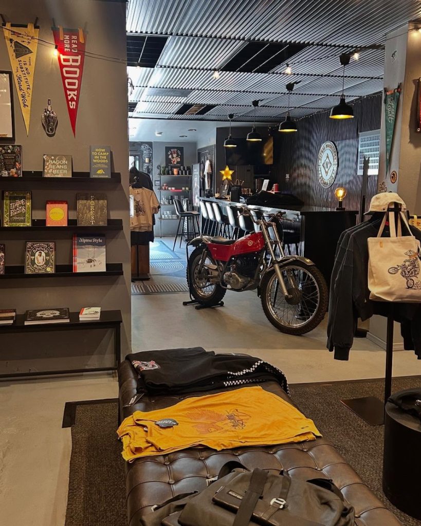 Interior of Mystic Moto in Big Bear featuring a vintage motorcycle, coffee bar, books, apparel, and a modern industrial-style retail space.
