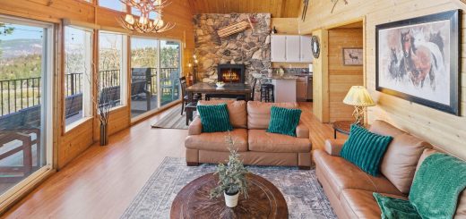 Nature's Dream cabin living room with leather sofas, stone fireplace, and open mountain view windows