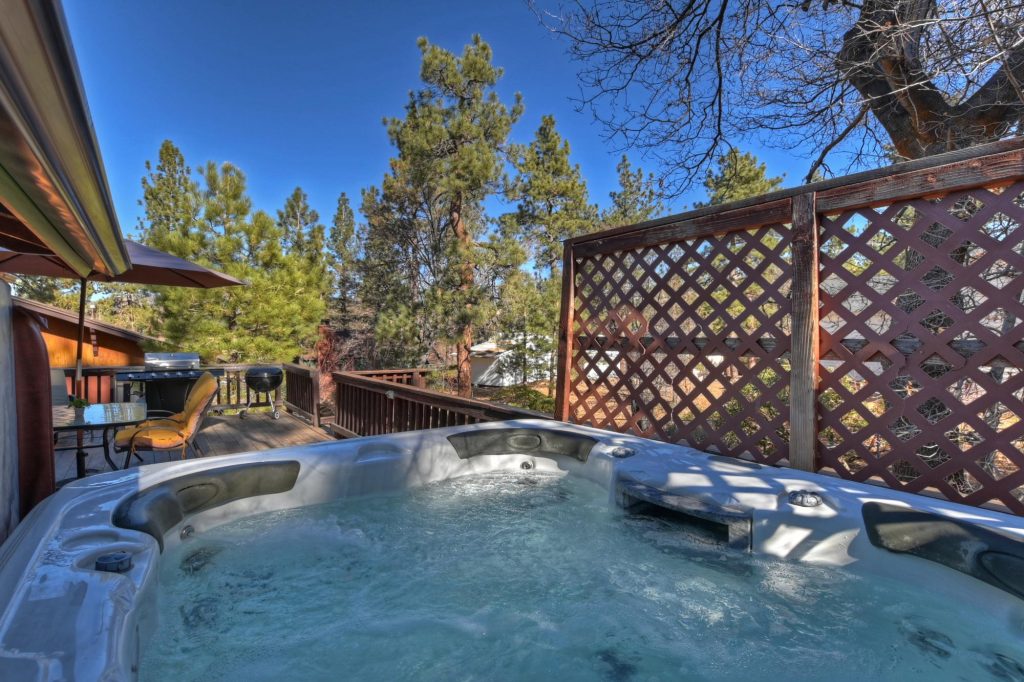 Outdoor hot tub on a wooden deck surrounded by pine trees with mountain cabin backyard view