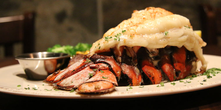 A cooked lobster tail on a white plate with greens in the back side of plate, inside a restaurant.