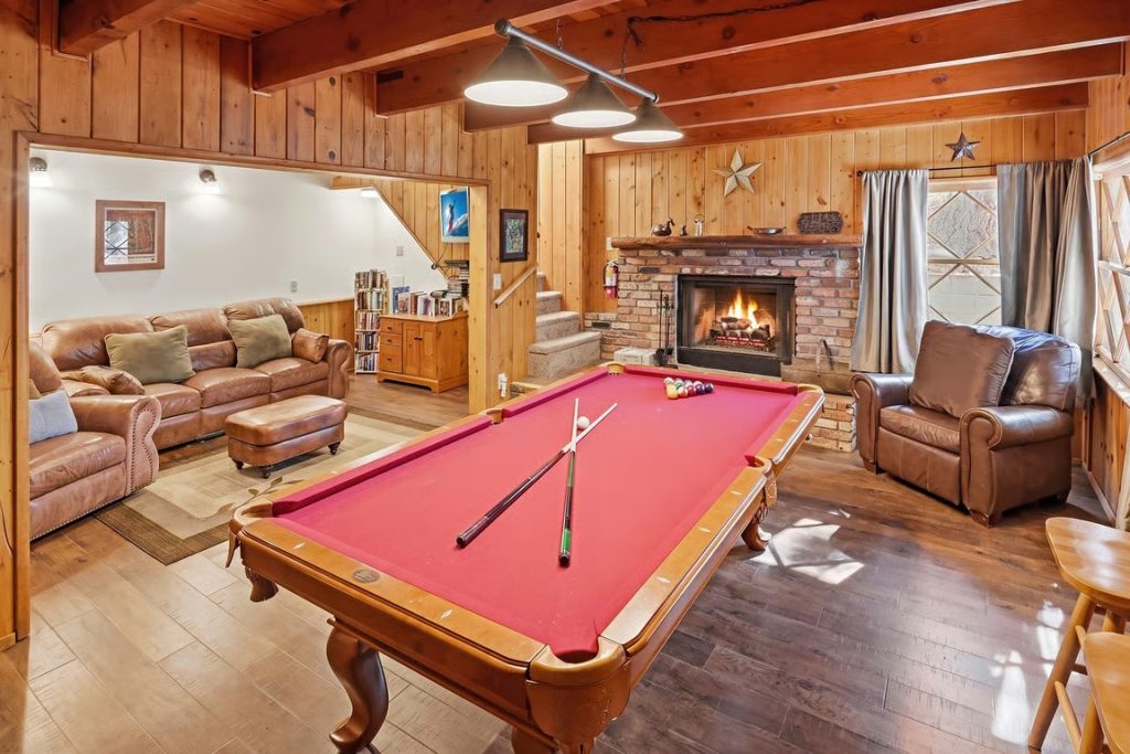 Cozy mountain cabin game room with a pool table, fireplace, leather seating, and wood-paneled interior