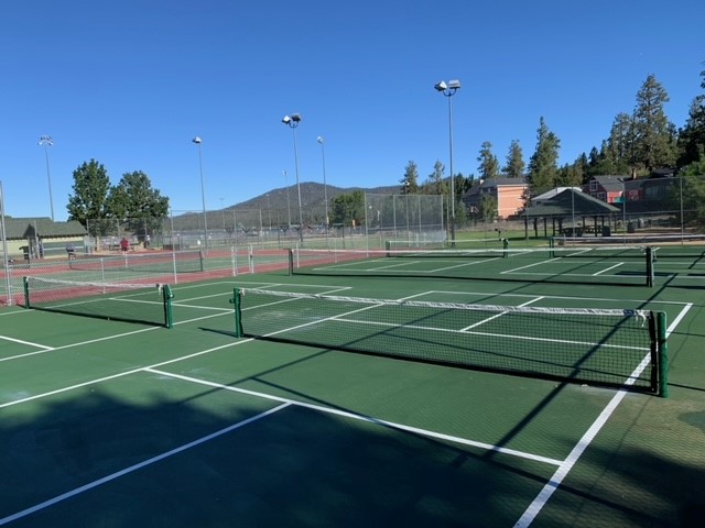 Outdoor pickleball courts with nets, fencing, and mountain surroundings under a clear blue sky.