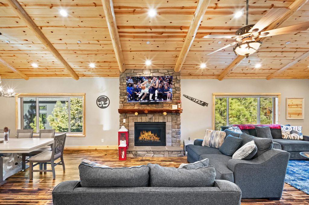 The interior of a modern cabin in Big Bear with a large living room, a stone fireplace, and a TV showing a basketball game.