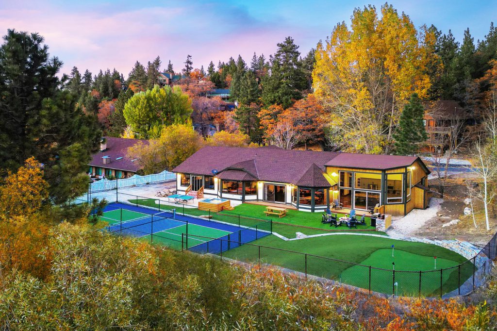 An aerial view of a pickleball court and a putting green next to a modern house in a wooded area in Big Bear.