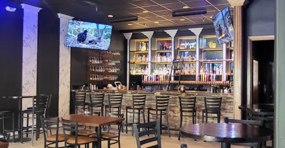 Modern bar area inside The Pita House featuring a full-service bar, comfortable seating, and televisions.